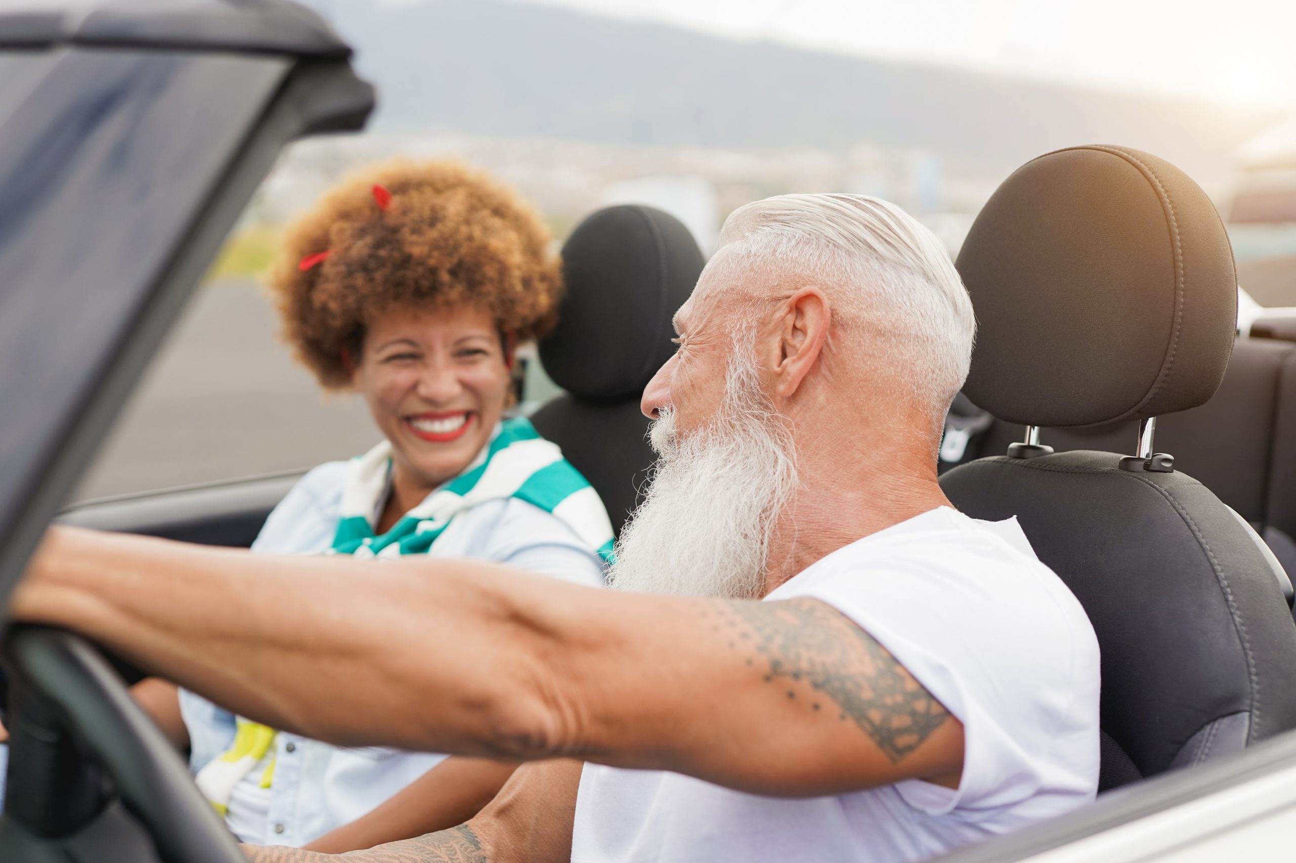 Mature couple having fun inside convertible car – Multiracial se